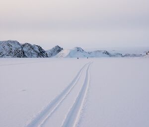 View down the snow-covered seaice of Long Fjord. Quad tracks and bikes in the far distance are visible.