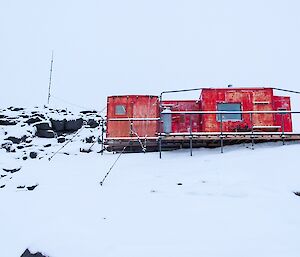The red building sitting on the snow and rock is Brookes Hut.