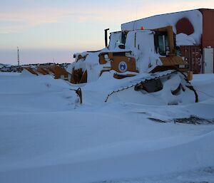 The bulldozer partially buried in snow.