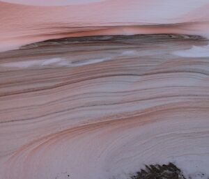 An abstract art shot of snow layered with sand, giving it pink and brown layers.