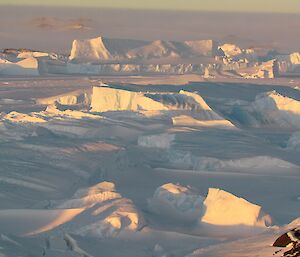 The icebergs frozen into fast ice between the island with Bandits hut and the plateau. Snow is seen blowing across the plateau down into the fjord.