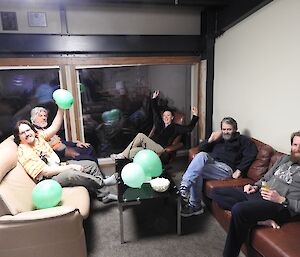 Team Green: Ralph, Richard, Daleen, Barry B2 and Sharky. Sitting on couches in another corner of the Living Quarters building holding green balloons.