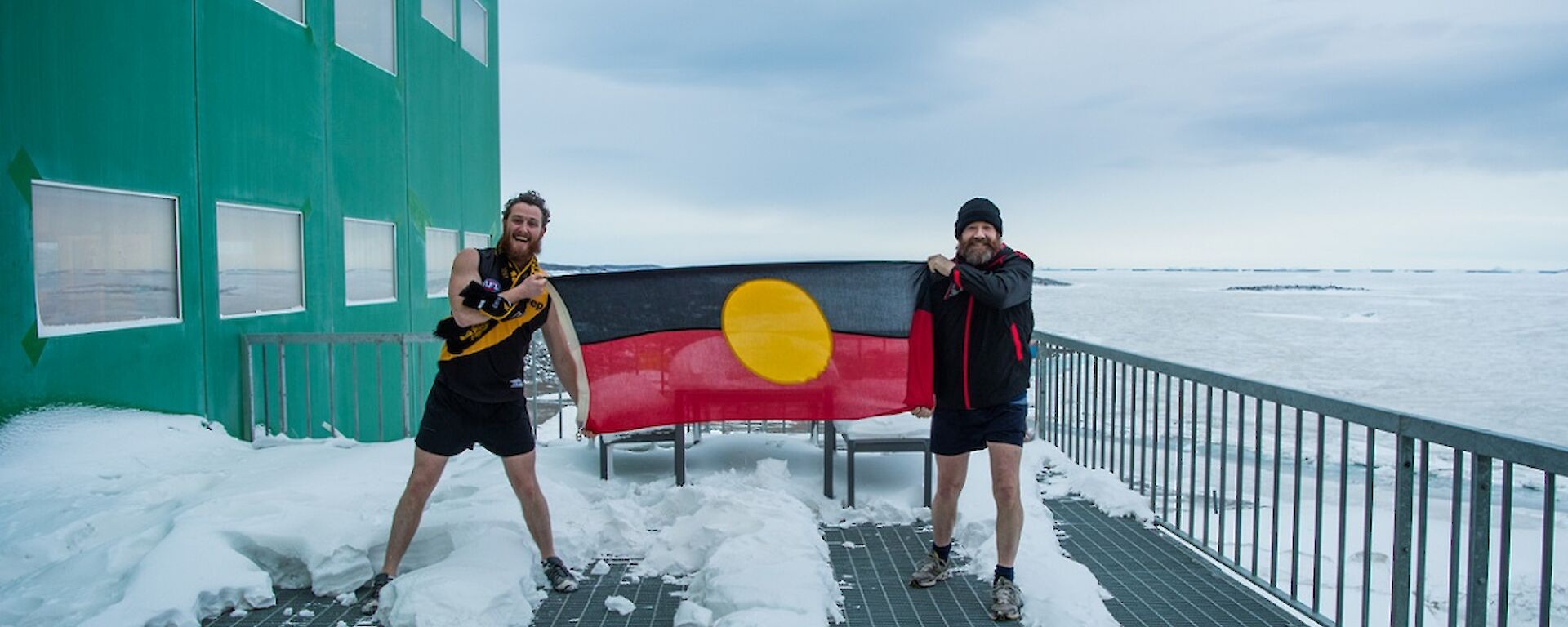 Bryce and Fitzy are holding the aboriginal flag in front on the Living Quarters building. Bryce is in Richmond gear while Fitzy is wearing Essendon gear.