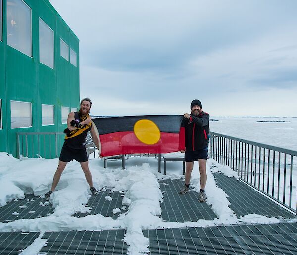 Bryce and Fitzy are holding the aboriginal flag in front on the Living Quarters building. Bryce is in Richmond gear while Fitzy is wearing Essendon gear.