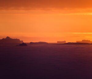 An orange sunset over the icebergs.