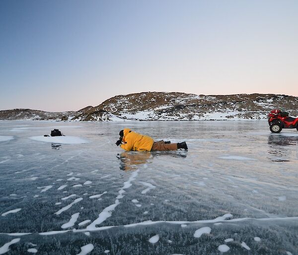 Barry (B1) is lying on the lake ice taking photos of the cracks in the ice. You can see a couple of quad bikes parked on the ice as well. Behind B1 are the Vestfold Hills and twilight skies.