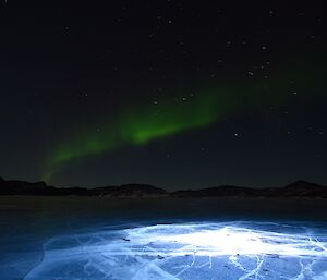 LED lit cracks in Lake Druzhby with a sneaky green aurora overhead.