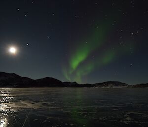 Auroras reflected on the lake ice. A bright moon is also present.