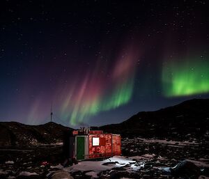 A magenta and green aurora lights up the sky over Watts hut.