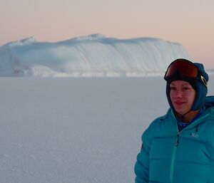 Daleen with a peachy sky and an iceberg in the background, during civil twilight.