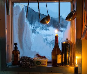 A Platcha still life photo with bottles and candles with snow on the window and condensation inside the cosy hut.