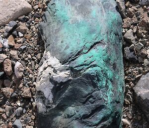 A grey rock with green copper extrusions.