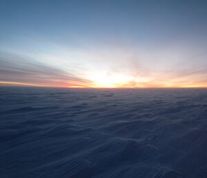 A landscape shot of the Antarctic plateau in twilight. Wind has blown the snow into sastrugi patterns but it is a hard surface, very cold at −30 degrees and there is a strong breeze.