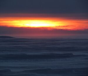 An orange glow from the sun is seen in the sky above the icy plateau. There was no sunrise but we enjoyed the colour in the sky.