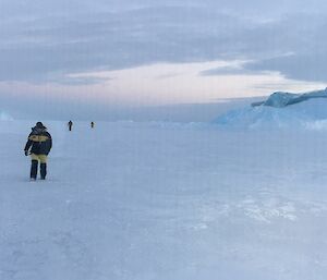 Three people are seen on the ice. They have walked around the jade berg which is seen to the right.