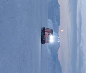 The pink Hägg is driving on sea ice, amongst the icebergs. The moon is seen above the Hägg.