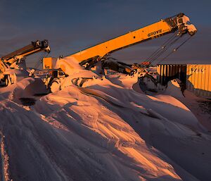 Blizzed machinery out on the snow at sunset.