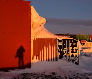 Barry’s shadow is seen against the boat shed. There is pink light on the snow surrounding the building.