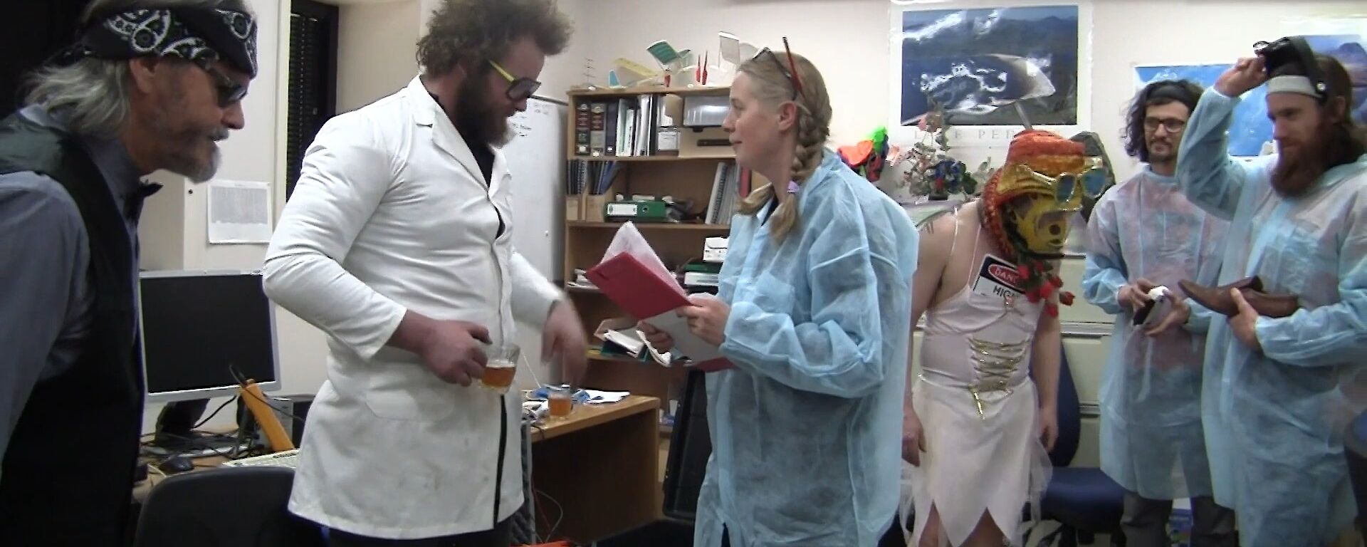 A party scene with a lab theme for the 48hr Film Festival. People are standing around in lab coats and protective clothing.