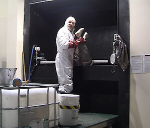 Fitzy is wearing a white protective suit and appears to be disposing of a “body” for the film scene.
