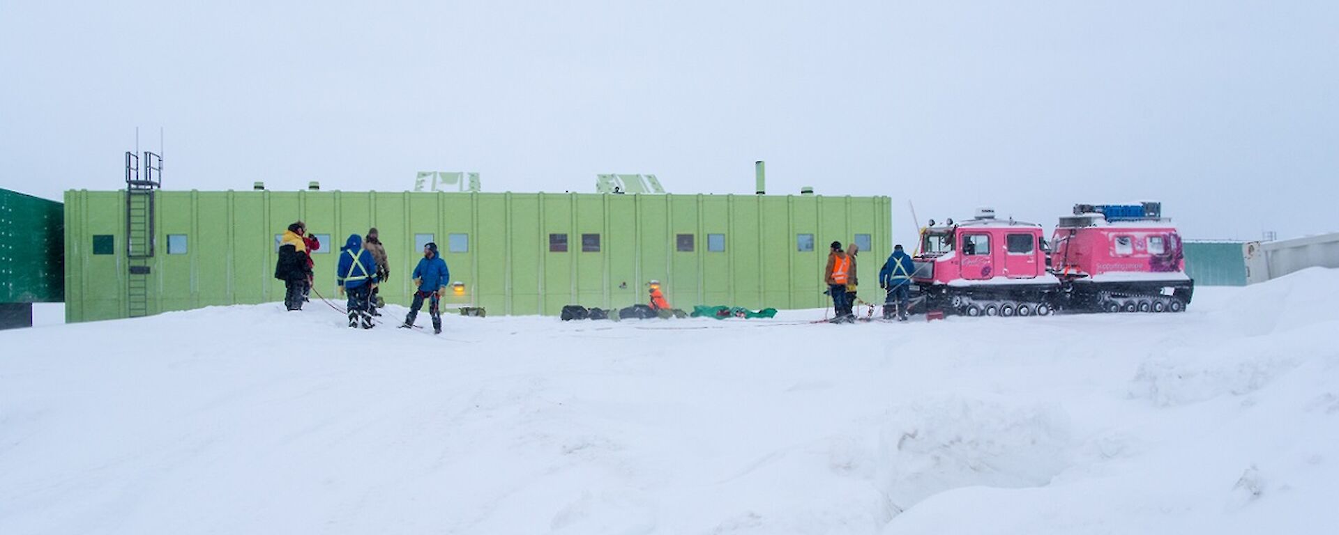 The Hägg is seen parked on the snow in front of the SMQ building. Ropes are strung out from the front of the vehicle as a rescue system. People are standing around working on the rope work.