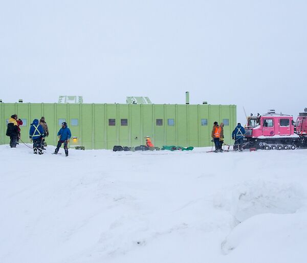 The Hägg is seen parked on the snow in front of the SMQ building. Ropes are strung out from the front of the vehicle as a rescue system. People are standing around working on the rope work.