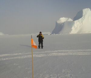 The Hägg on the sea ice with an iceberg in the background. There is a flag indicating that it is a site for measuring sea ice thickness.