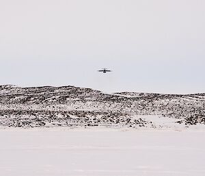 The plane is flying over the hills, about to fly over the drop zone out on the sea ice.