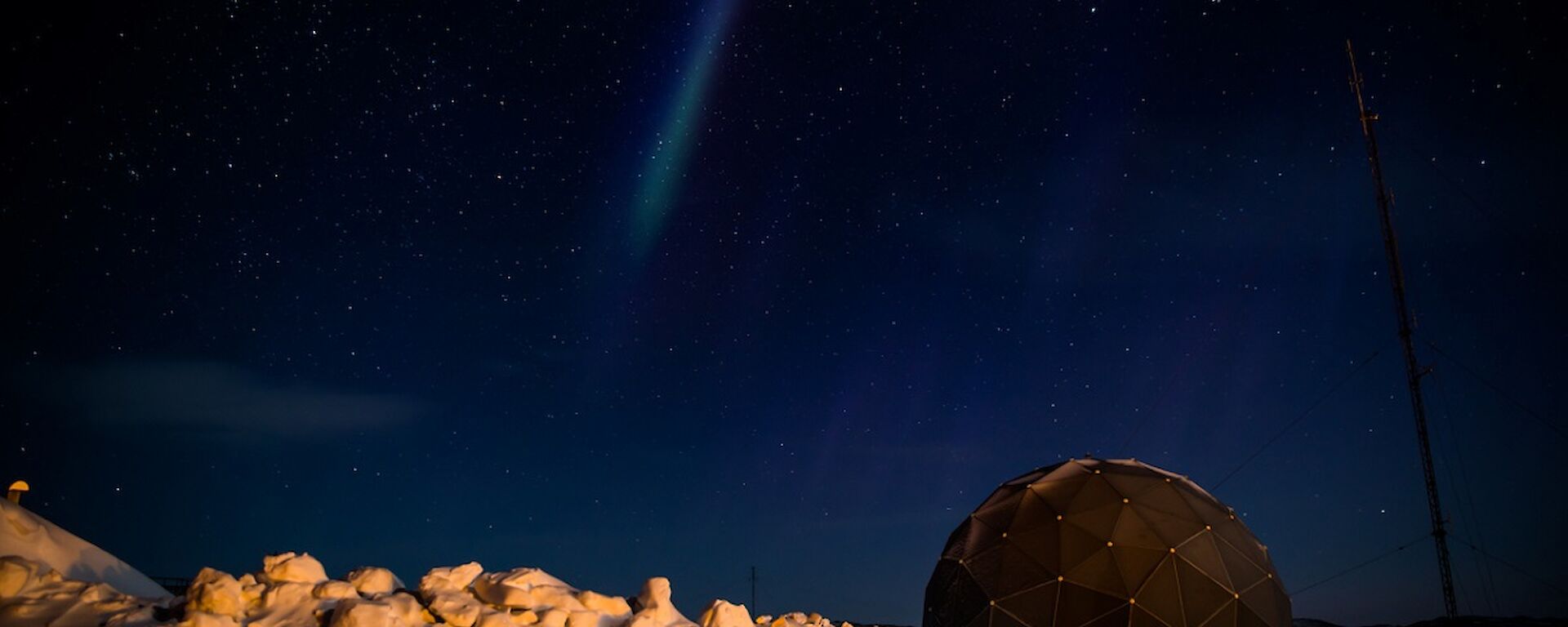 Moonlit snow under a starry sky with a weak aurora by the satellite dome.