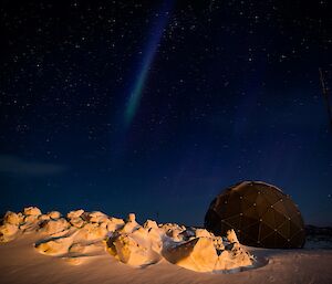 Moonlit snow under a starry sky with a weak aurora by the satellite dome.