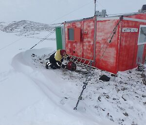 Rhys is bent over a generator outside Watts hut, trying to get it working.