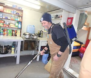 Barry B1 is vacuuming inside Watts hut. You can see the kitchen facilities behind him and the sleeping area to the right.