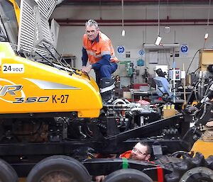 Barry B2 and Millsy are working on the groomer inside the workshop. Some of the casing has been removed so they can access the engine and track wheels.