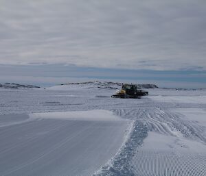 A groomer is seen pushing snow around. Areas already groomed are corregated and smoother than the surrounding sea ice.