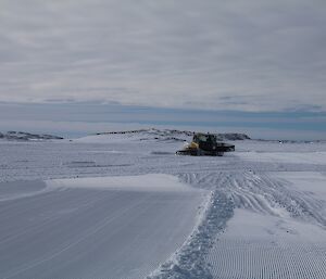 A groomer is seen pushing snow around. Areas already groomed are corregated and smoother than the surrounding sea ice.