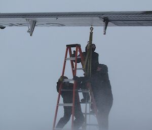 Doug, Ryan and Jeff attempt to reattach the Twin Otter’s wing tie down in the blizzard. Ryan is up on a ladder under the wing while the others anchor the ladder in the high wind.