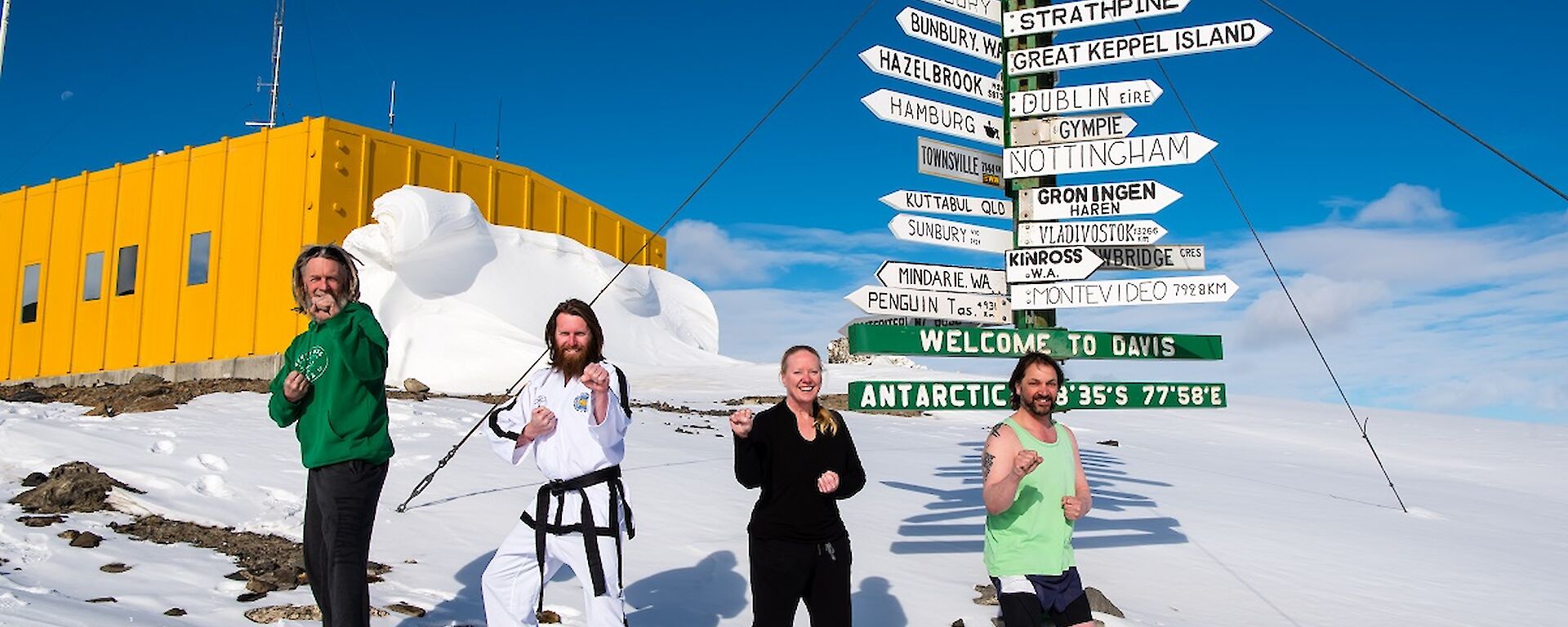 Four people standing outside next to a sign holding a taekwondo class