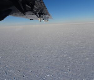 View of ice with blue sky above, and a small section of a plane wing in the top right hand corner.