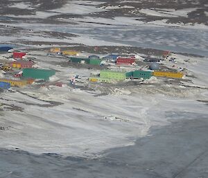 Photo of Antarctic station with lots of colourful building and melting snow revealing brown patches of dirt.