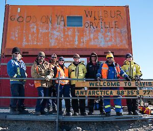 People standing in front of stacked shipping containers with a welcome sign.