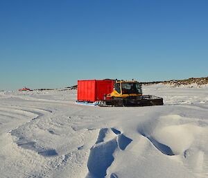 A tracked snow vehicle tows a sled with container on it across the ice.