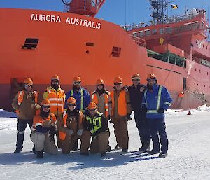 A group of workers pose in front of the ship parked in ice.