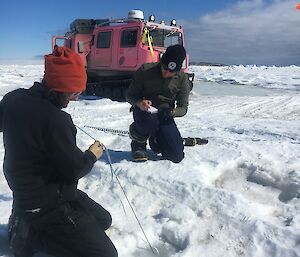 Two men measure ice thickness through a hole in the ice.
