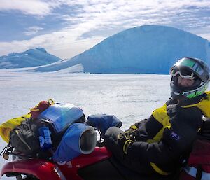 A woman sits on a quad bike in front of an iceberg.