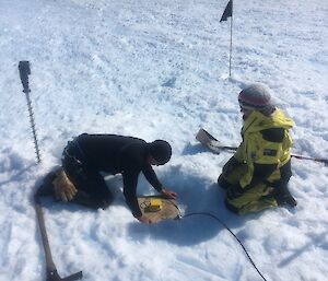 Two people place an instrument on the snow.