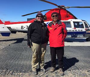 A man and woman stand in front of a helicopter.