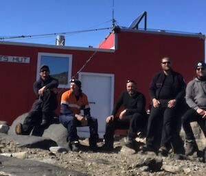 5 men in front of a hut