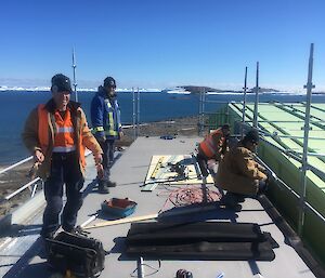 4 men repair a roof with icebergs in the distance