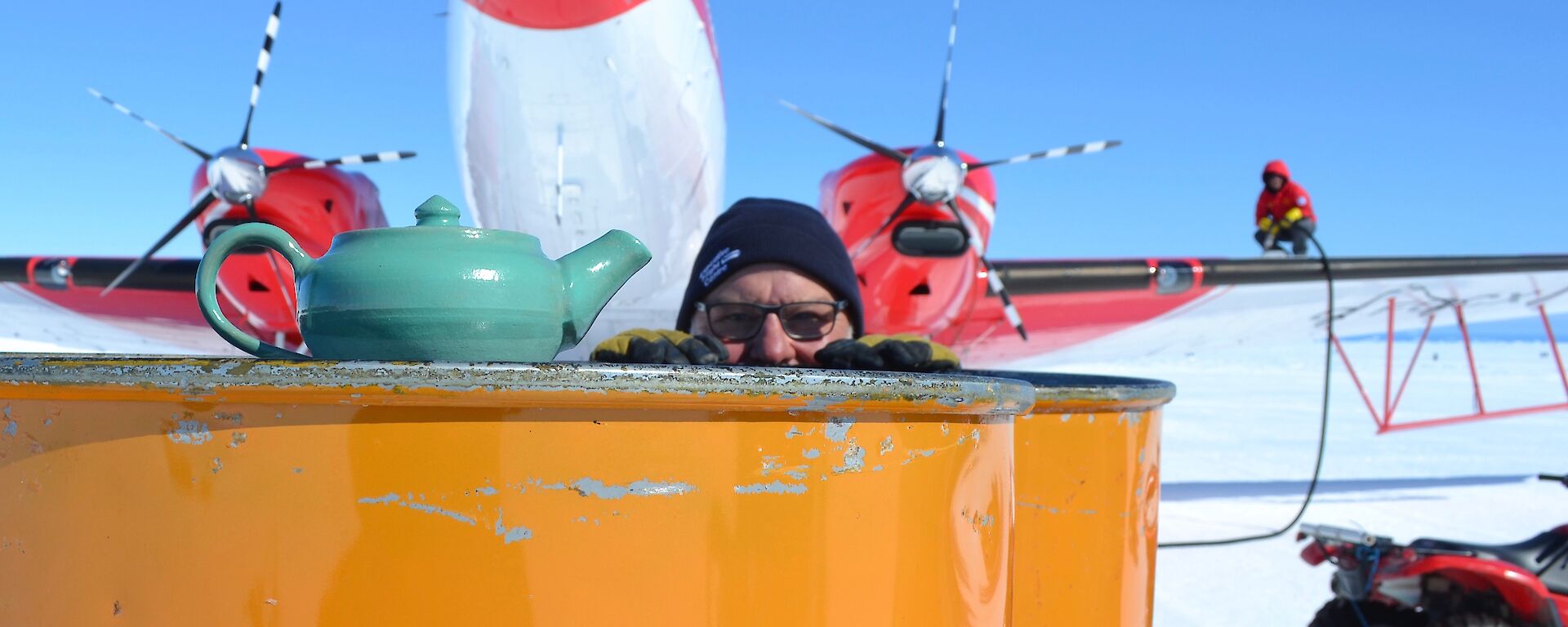 A man looks at a tea pot in front of an aeroplane