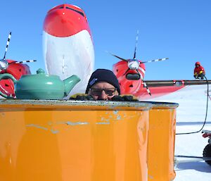 A man looks at a tea pot in front of an aeroplane